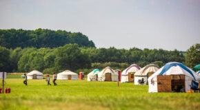 Traditional yurts with different colours are spaced out in Kelmarsh Estate, with trees in the background.