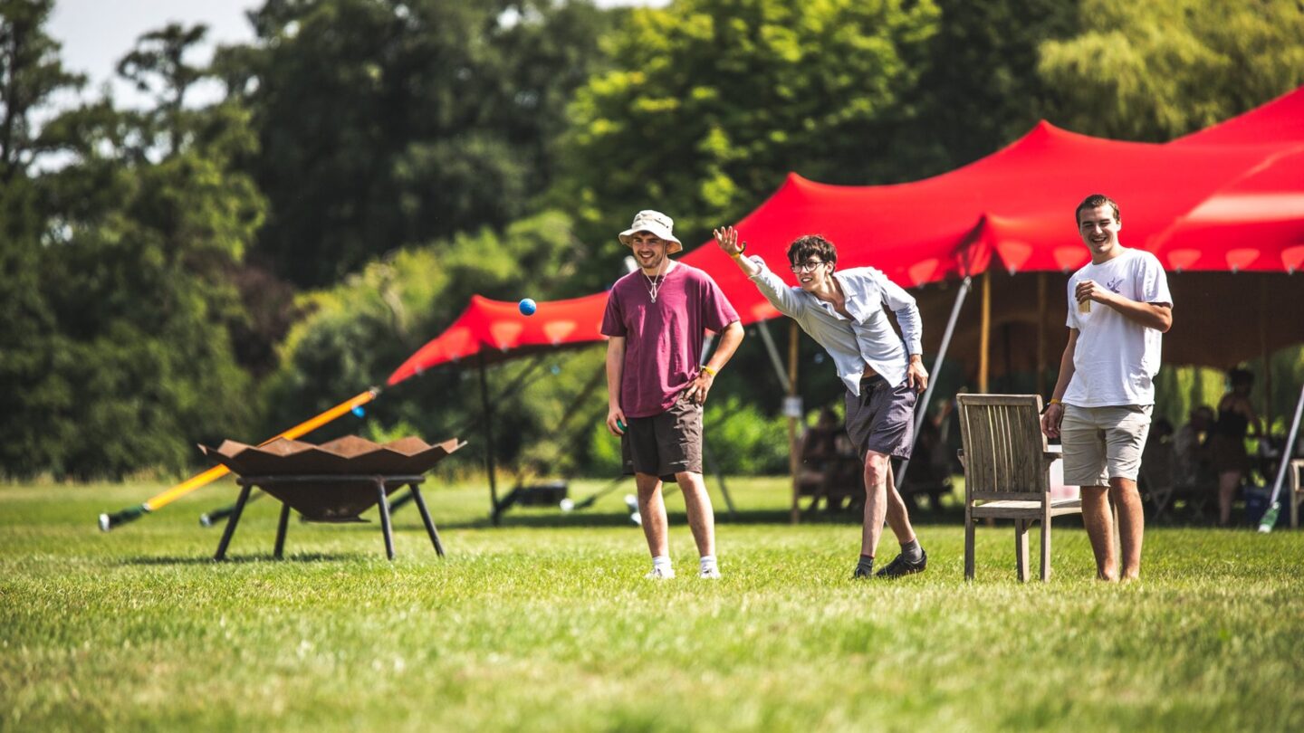 Three men stand in a row playing boules on the green