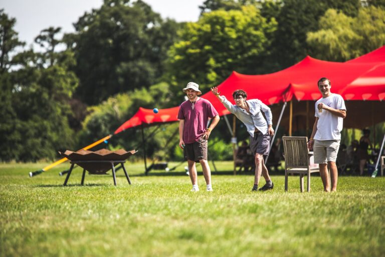 Three men stand in a row playing boules on the green