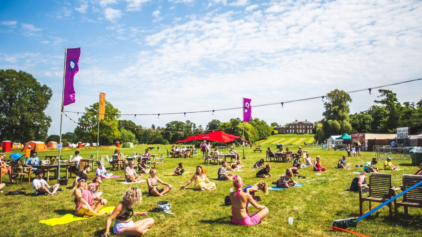 A group of people participate in socially distanced yoga in the meadow overlooking Kelmarsh Hall