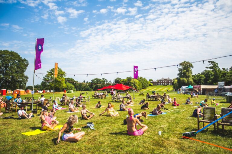 A group of people participate in socially distanced yoga in the meadow overlooking Kelmarsh Hall