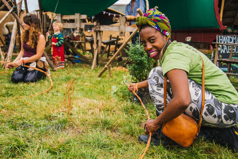 A woman with a headscarf smiles as she crafts with willow