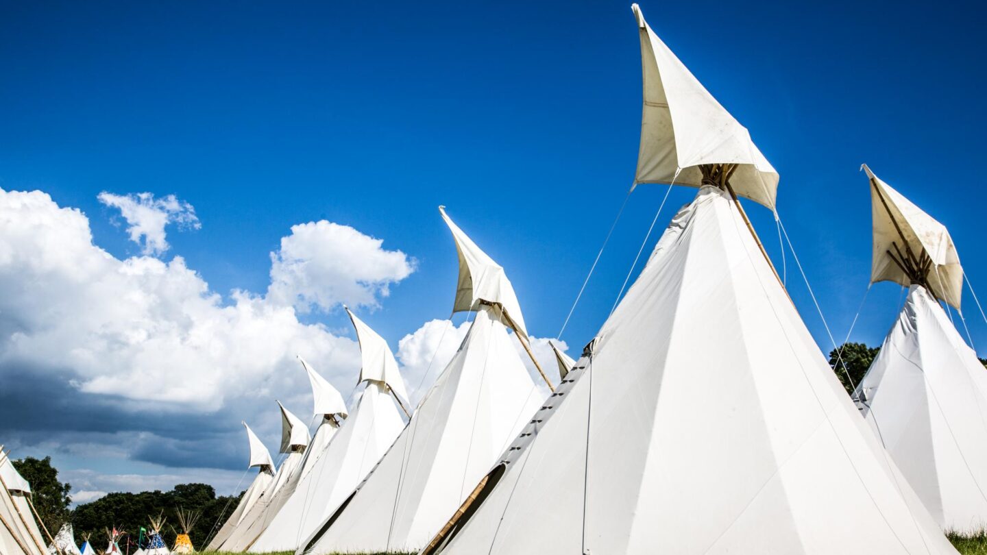 A row of beautiful handcrafted traditional tipis against a bright blue sky.