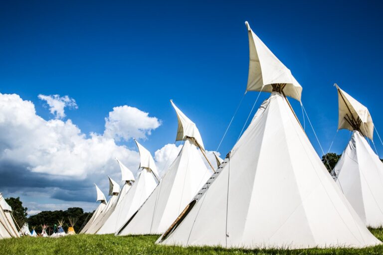 A row of beautiful handcrafted traditional tipis against a bright blue sky.